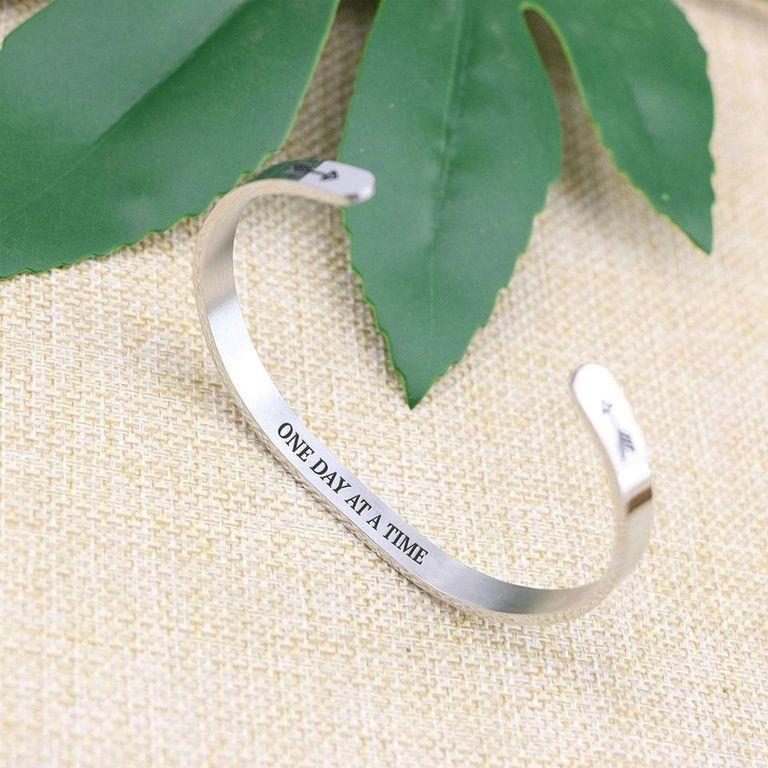 One day at a time bracelet with silver plating standing on a burlap surface with a leafy background