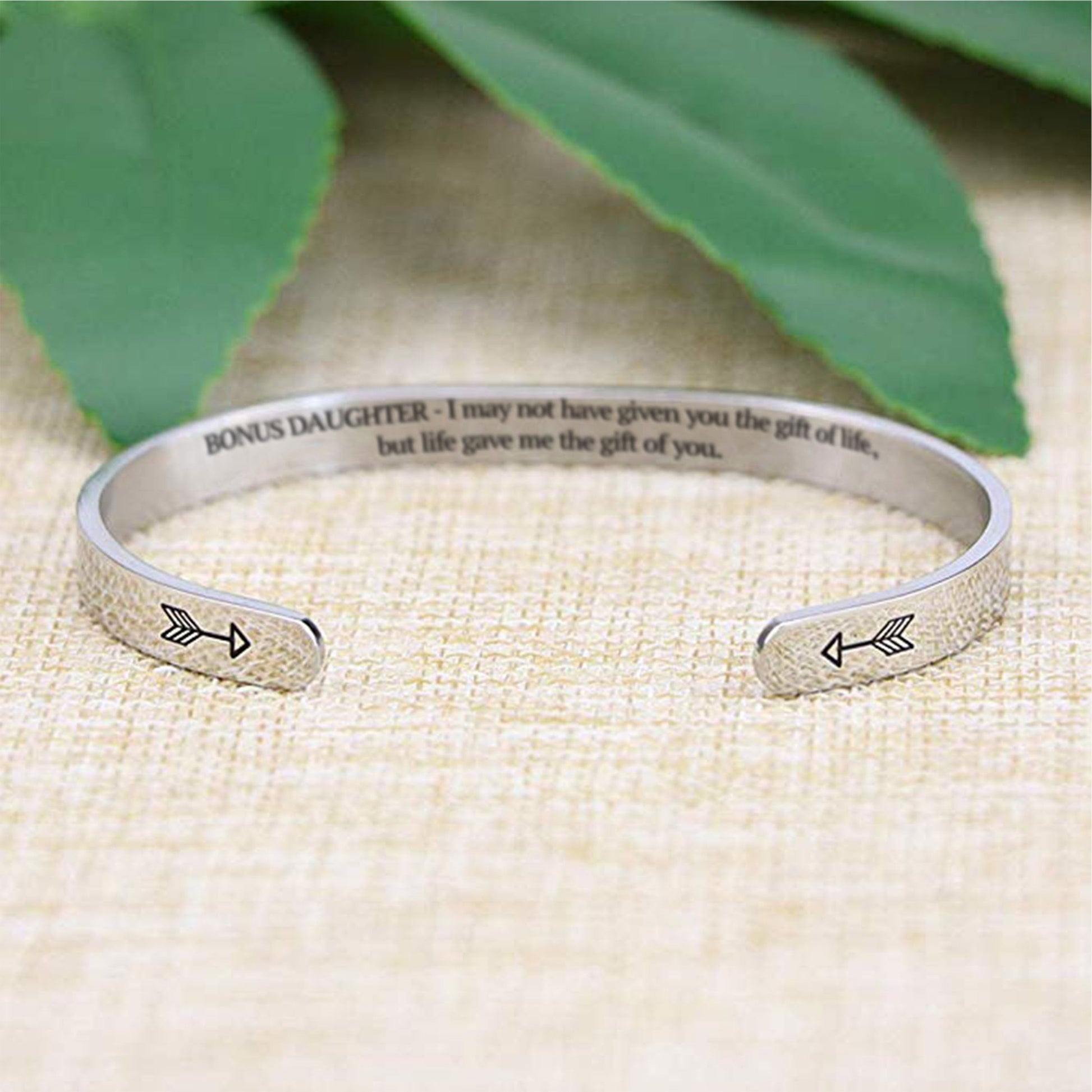 I may not have given you the gift of life but life gave me the gift of you bracelet with silver plating with arrows in focus on a burlap surface with a leafy background